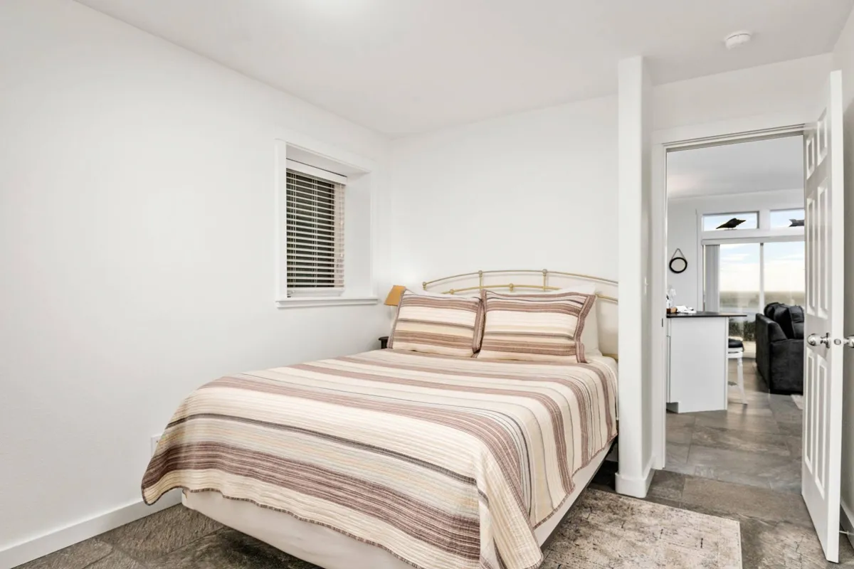A tranquil bedroom with a king-size bed dressed in striped bedding, a window allowing in natural light, and a serene atmosphere perfect for rest and relaxation.
