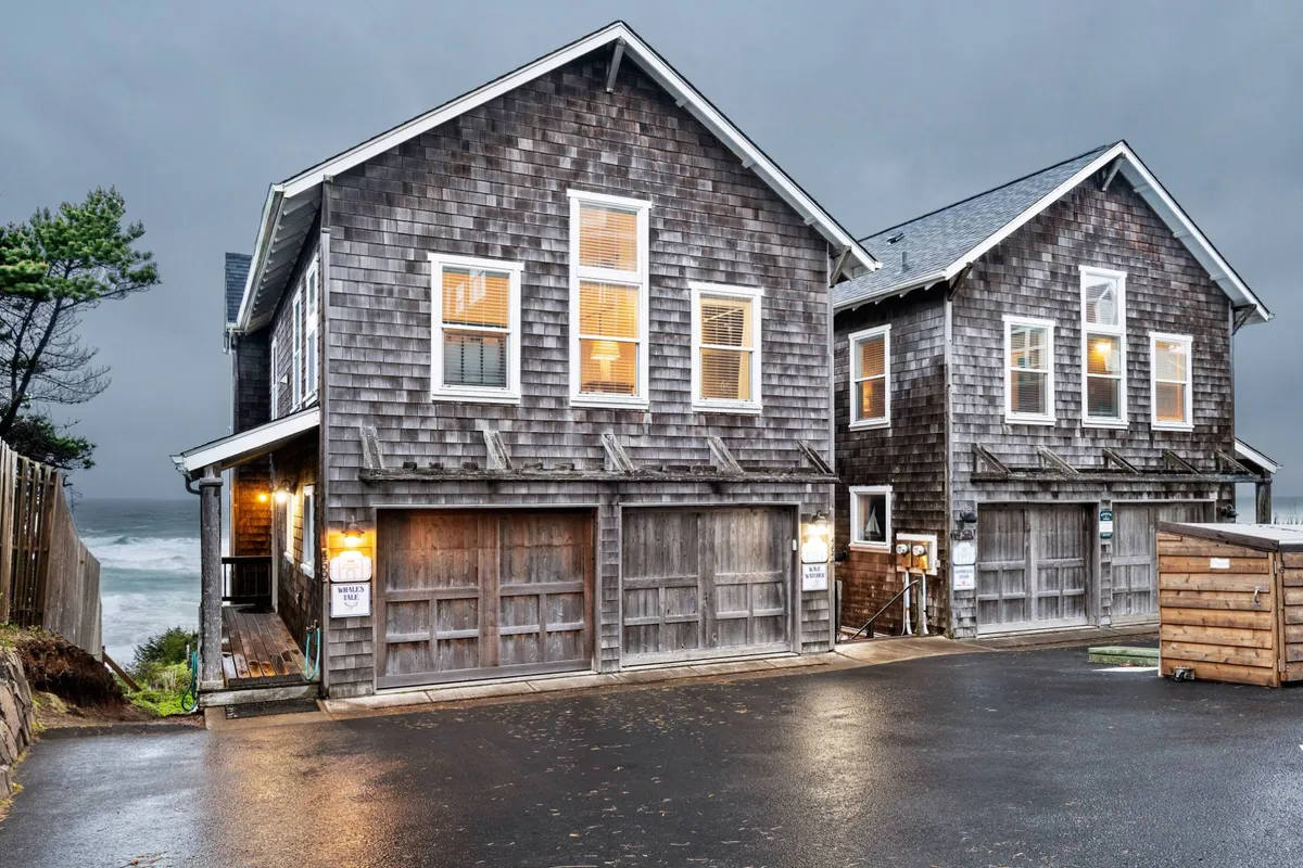 A serene exterior showing the wooden shingle facade of the property, large windows, and a tranquil ocean backdrop. The mood is peaceful, with hints that the home is nestled right by the beach, ideal for walks or family gatherings at sunset.