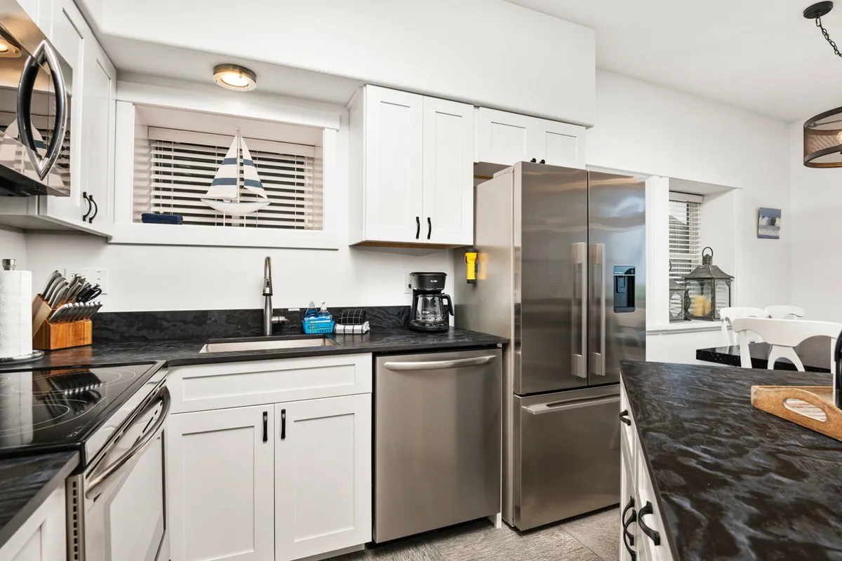 A welcoming kitchen featuring stainless steel appliances, a modern black countertop, crisp white cabinetry, and a decorative sailboat perched on a shelf. The space feels bright and functional, perfectly suited for preparing meals or gathering with family.