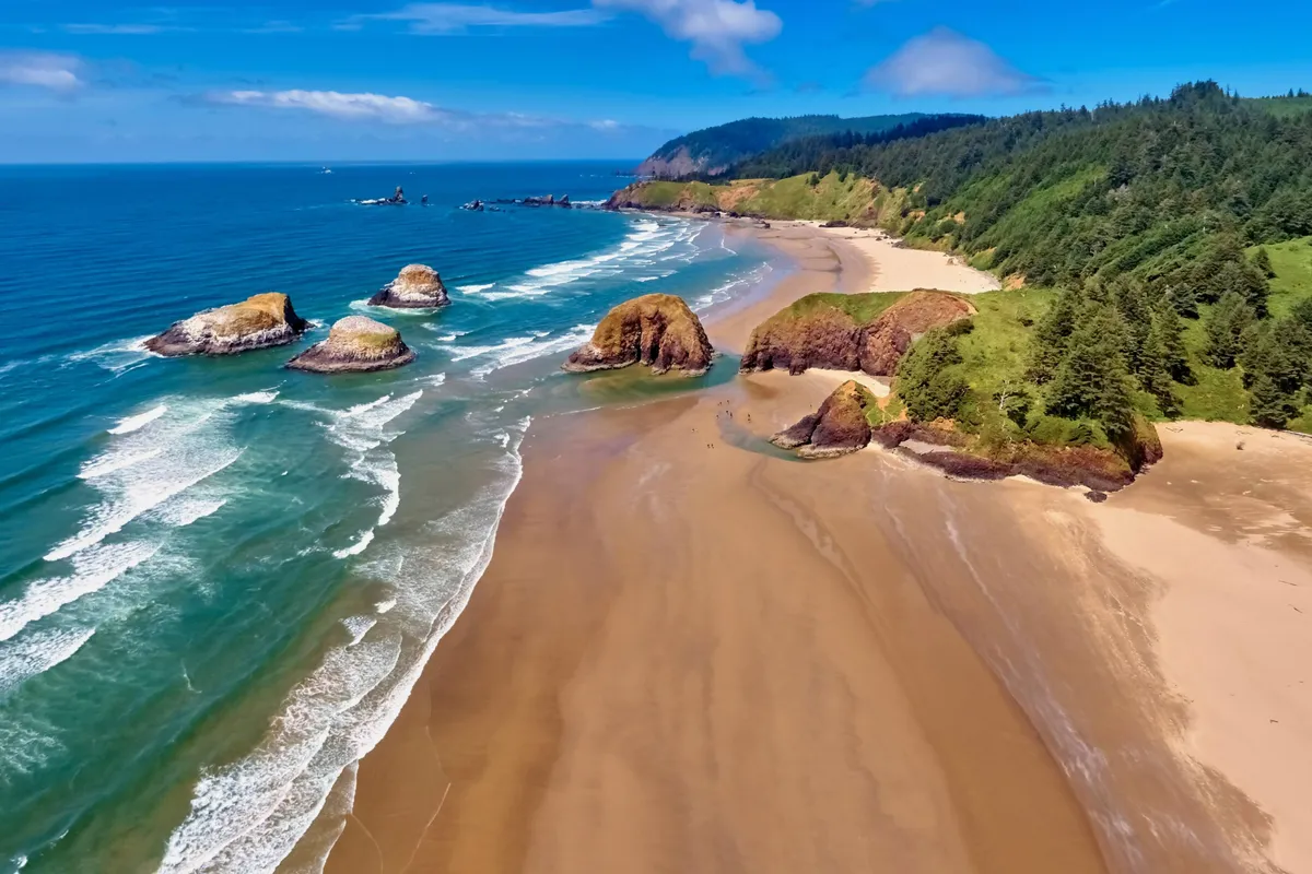 A sweeping view of the sandy beach with dramatic rock formations, gentle waves, and lush greenery in the background. The scene invites exploration and highlights the natural beauty awaiting just outside the property.