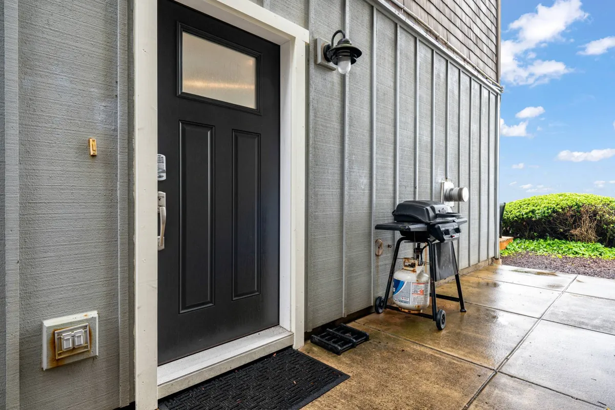 An inviting outdoor area featuring a grill and comfortable seating near the front door of the home. The space is set up for barbecuing and socializing, suggesting the perfect spot for casual group meals or evening gatherings under the stars.