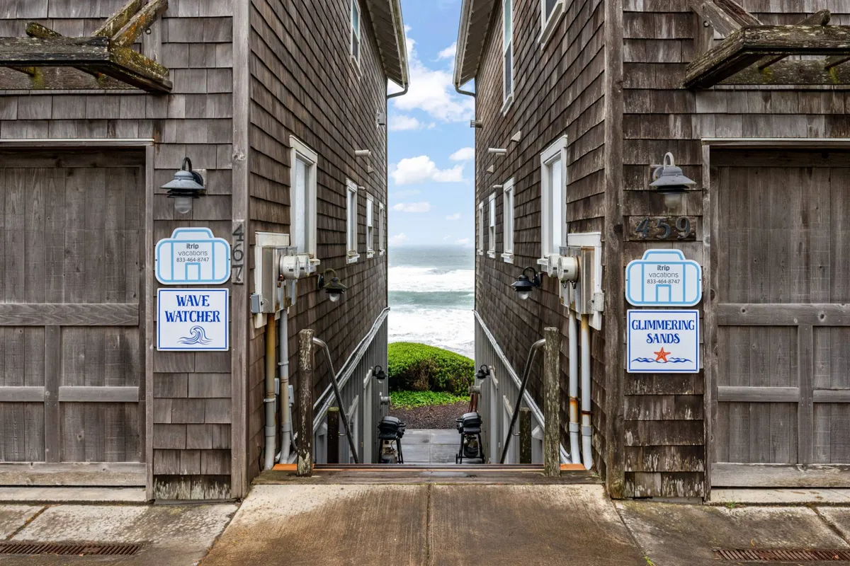 This image captures a serene view of wooden structures and signage overlooking the ocean, with the sandy beach just beyond. The scene is tranquil, evoking the experience of stepping outside and being just moments from the water's edge.