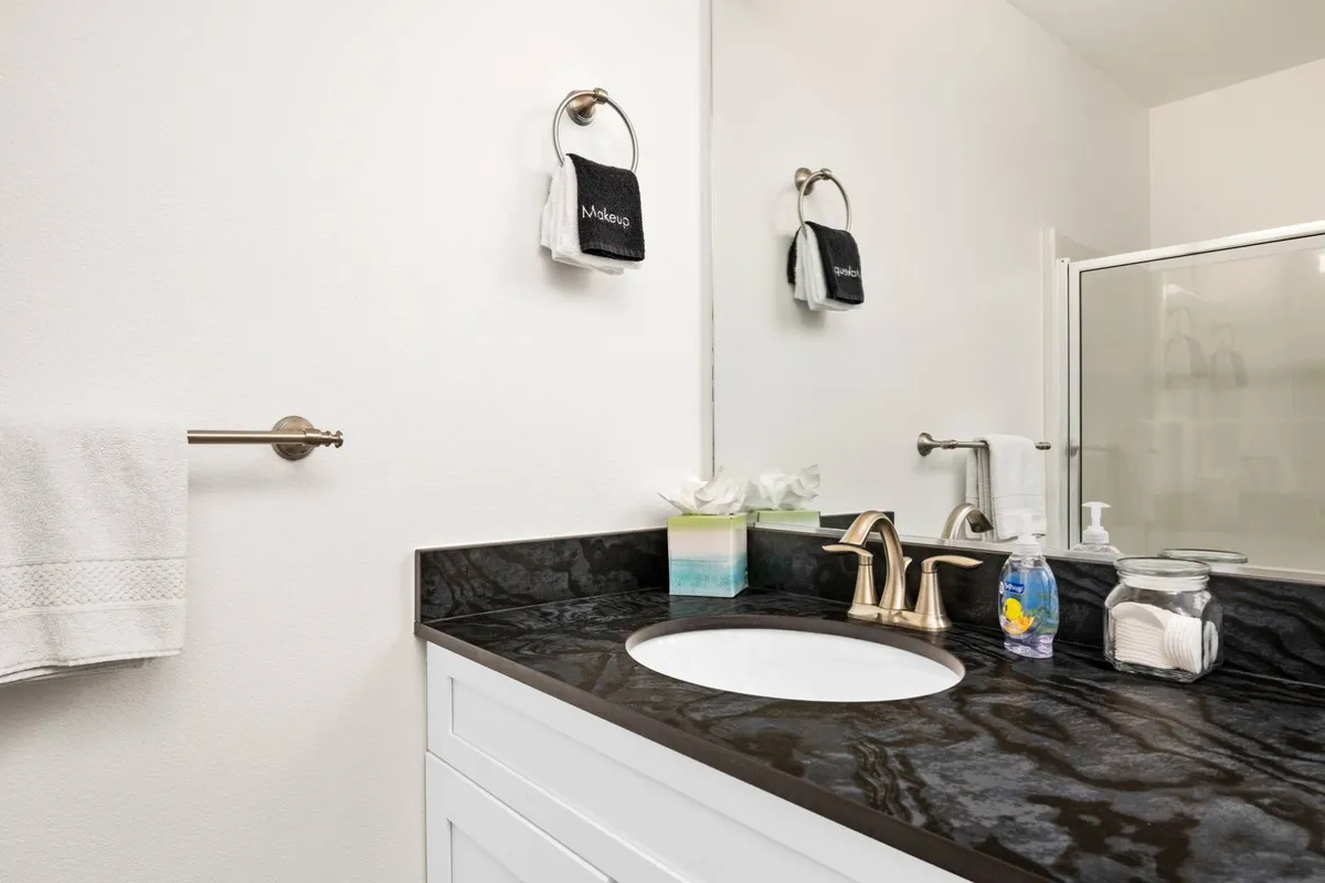 A modern en-suite bathroom featuring a sleek vanity with a dark countertop, a large mirror, and neatly arranged towels, evoking a sense of relaxation and practical luxury.