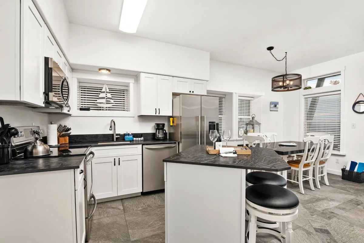 A spacious kitchen and dining area with a central island, stainless steel appliances, an adjacent dining table, and a modern light fixture overhead. The open layout supports easy conversation and flow between cooking, dining, and socializing.