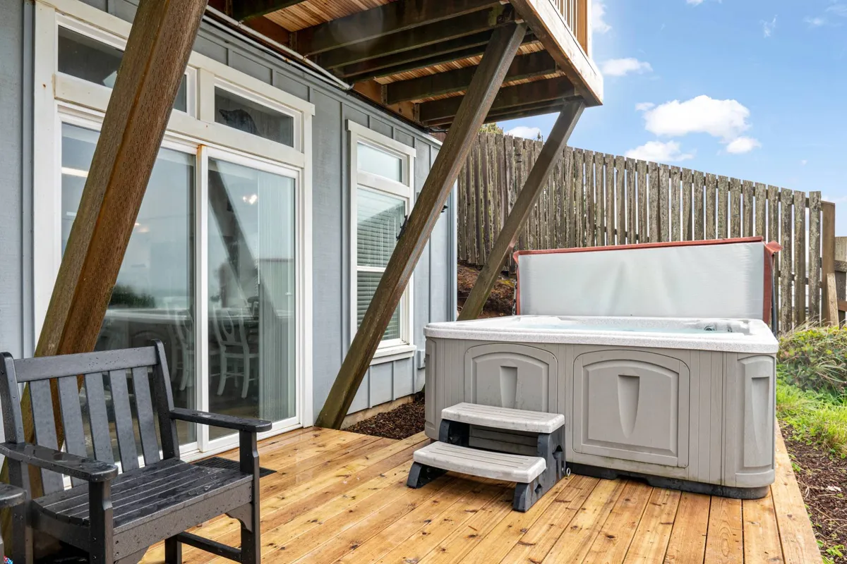 A tranquil wooden deck with an inviting hot tub overlooking the ocean, surrounded by comfortable outdoor seating. The scene promises relaxation and privacy, ideal for unwinding while listening to the waves.