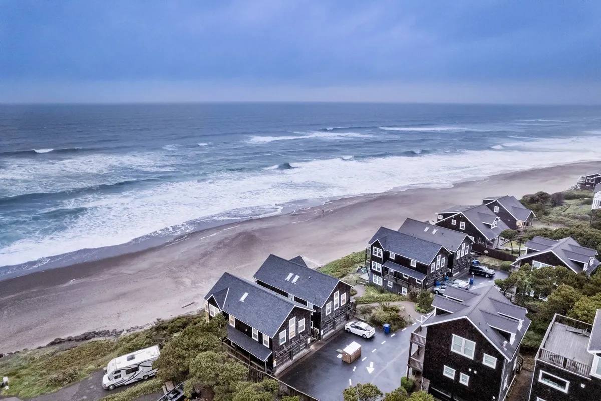 This serene view captures the wide sandy beach, rolling ocean waves, and neighboring beach houses, evoking the essence of a coastal family vacation. The scene is peaceful, with families and groups enjoying the shore, suggesting opportunities for sandcastles, beachcombing, and relaxing.