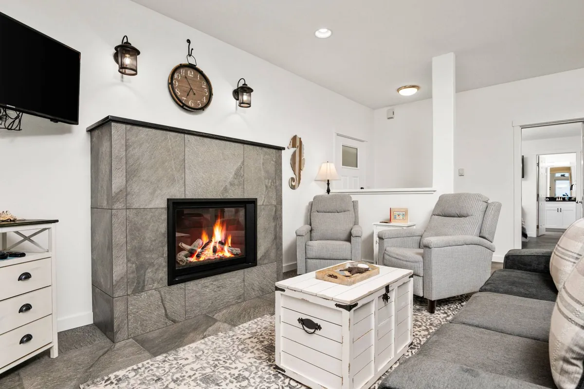 A cozy living room interior featuring a fireplace, comfortable armchairs, and a coffee table. The setting is designed for relaxation, socializing, and enjoying warm evenings indoors.